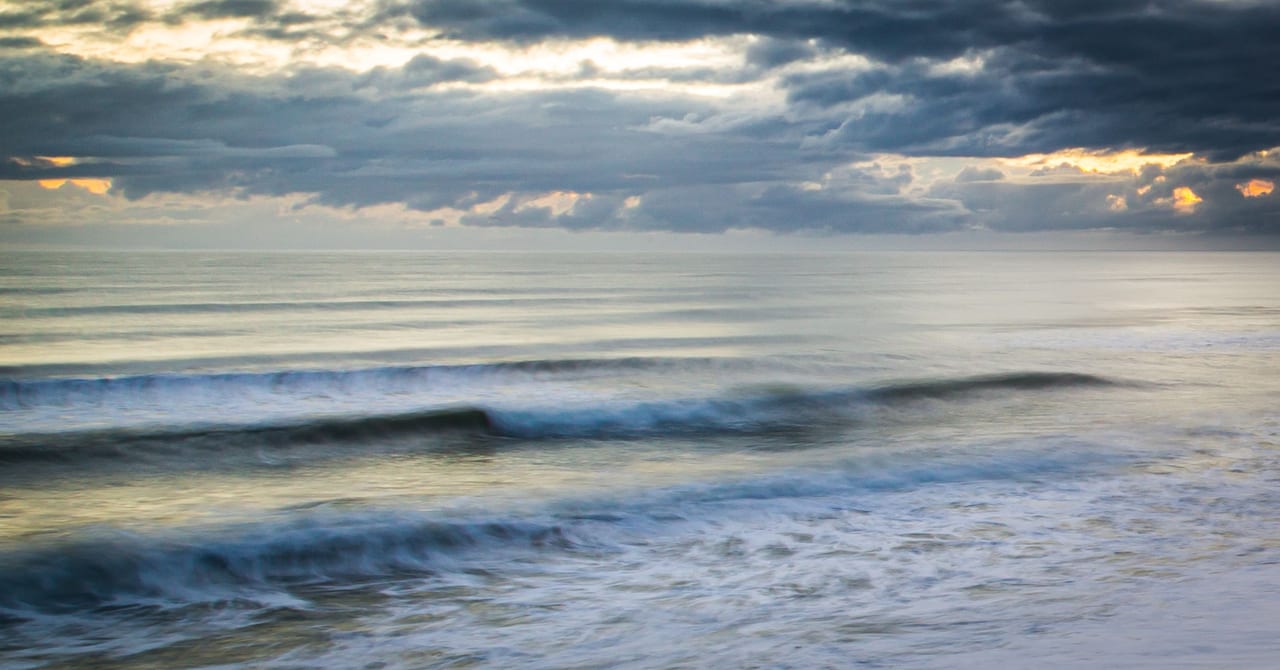 Gentle waves lapping at a calm ocean under a cloudy sky at dusk.