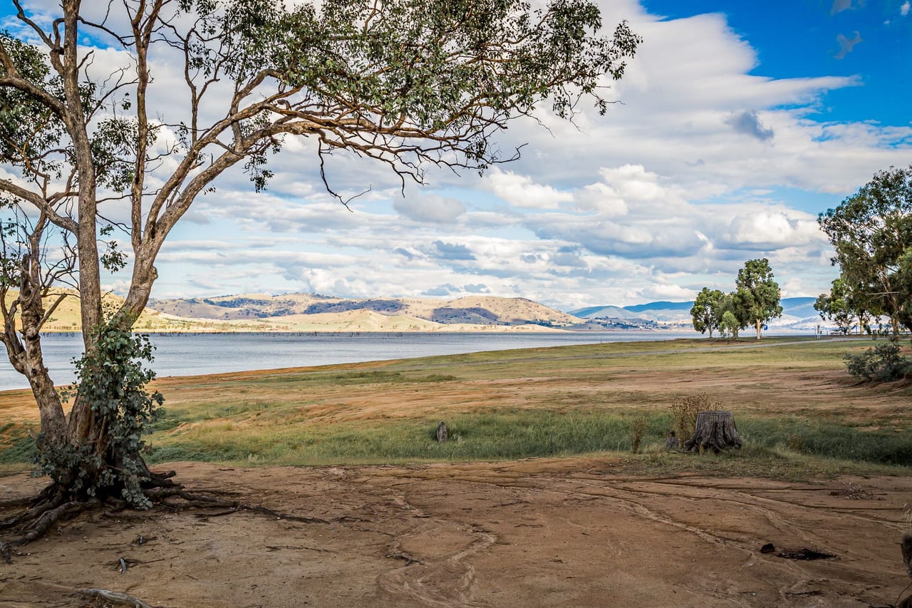 A serene view of a lake surrounded by trees and hills under a cloudy sky.