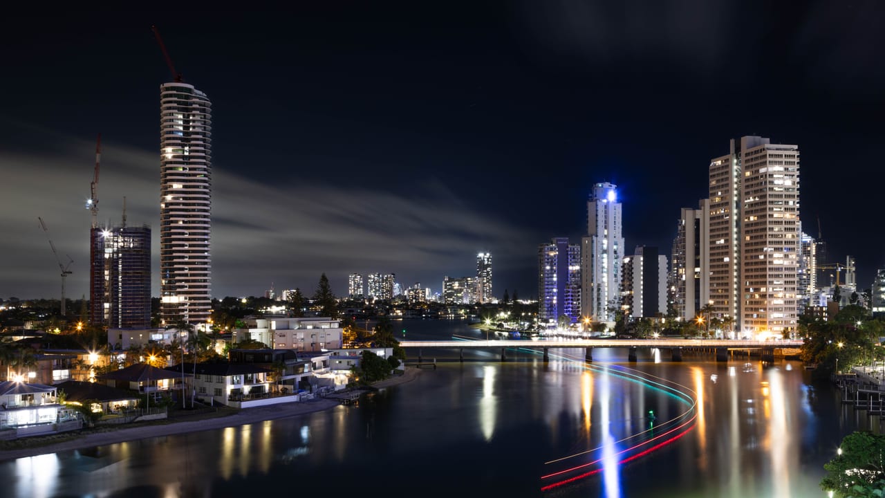 Nighttime cityscape with illuminated buildings beside a river.