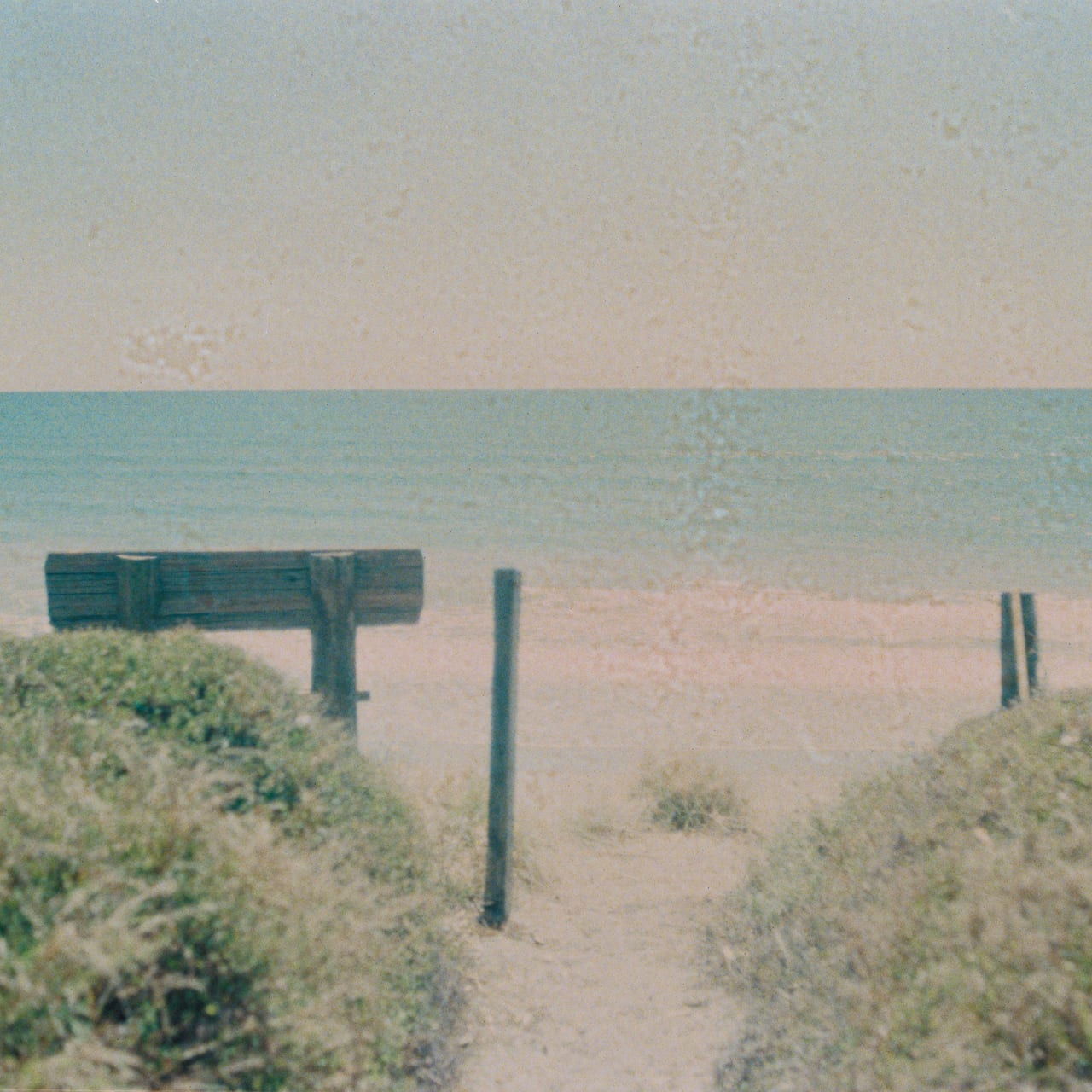 A wooden path leading to a calm beach with the ocean in the background.