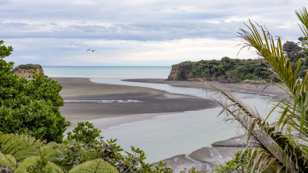 A serene river mouth meeting the sea, surrounded by greenery and cliffs.
