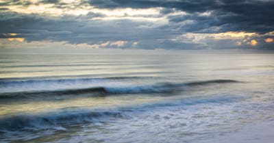 Gentle waves lapping at a calm ocean under a cloudy sky at dusk.