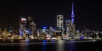 A wide view of Auckland's skyline illuminated at night with the Sky Tower visible.